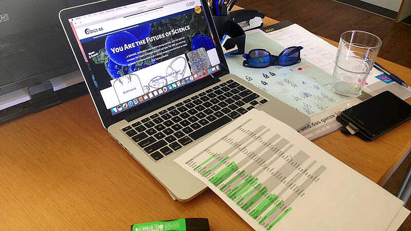 Picture of a desk with a laptop, a sheet of paper, and different office stuff
