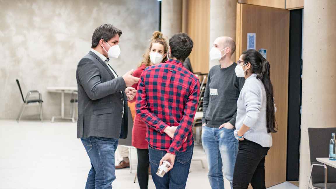 A group of people with face masks, standing around in a group talking to each other